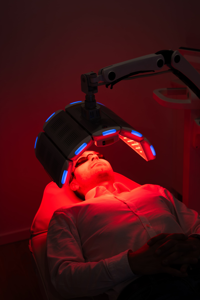 Man lying on treatment bed receiving red light therapy on face with protective goggles