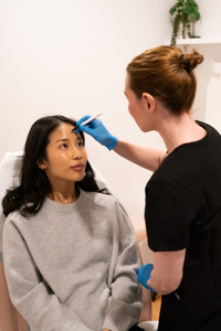 Clinician wearing blue gloves marking a woman's forehead in a treatment room