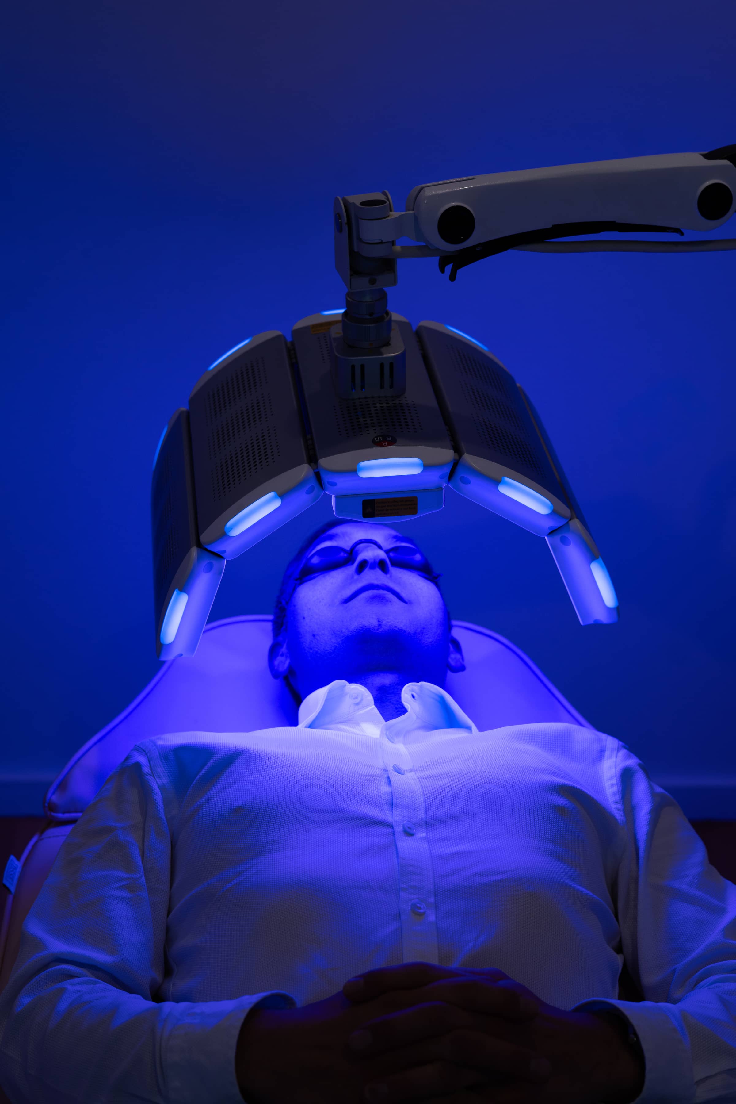Man wearing protective goggles receiving blue light skin treatment while lying on clinic bed